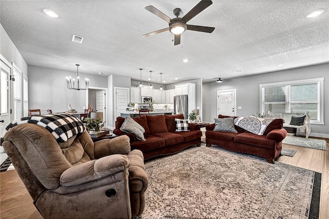 living room with ceiling fan with notable chandelier, recessed lighting, wood finished floors, and a textured ceiling