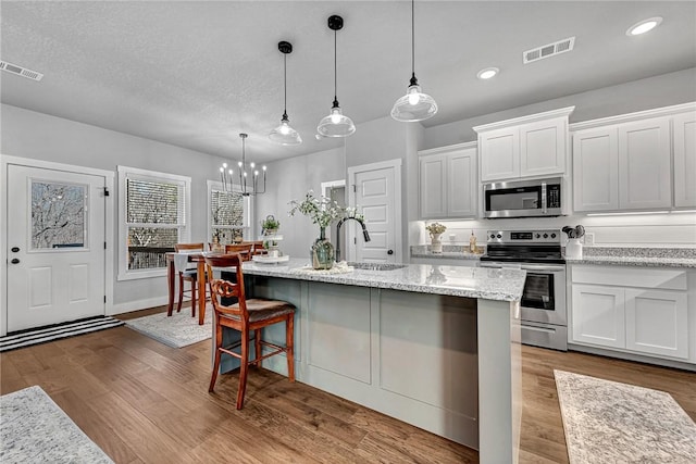 kitchen with stainless steel appliances, visible vents, wood finished floors, and white cabinets