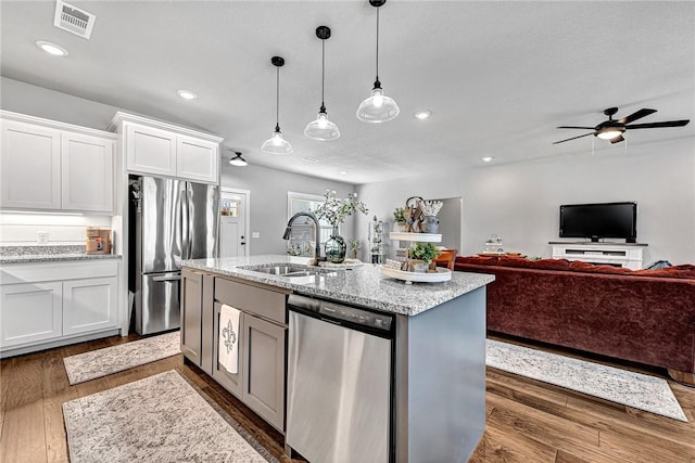 kitchen featuring light stone countertops, dark wood-style floors, a sink, stainless steel appliances, and white cabinetry