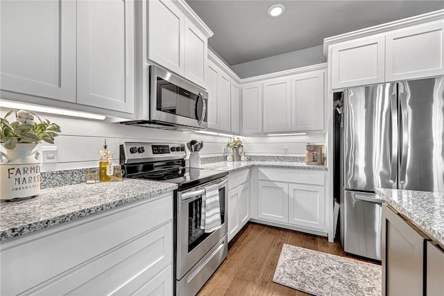 kitchen featuring light stone counters, wood finished floors, recessed lighting, appliances with stainless steel finishes, and white cabinets