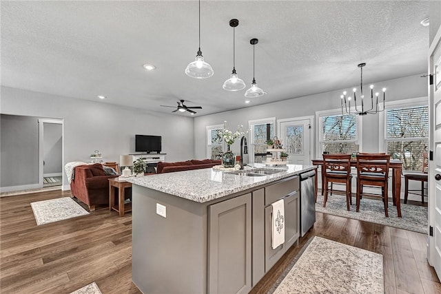 kitchen with a sink, light stone counters, stainless steel dishwasher, a textured ceiling, and dark wood-style floors