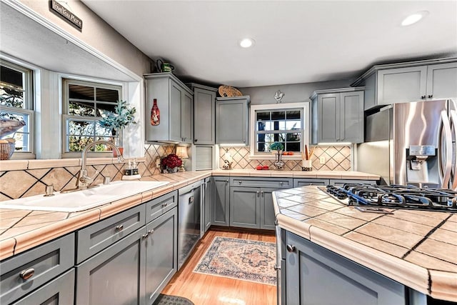 kitchen with stainless steel appliances, tile counters, a sink, and gray cabinetry