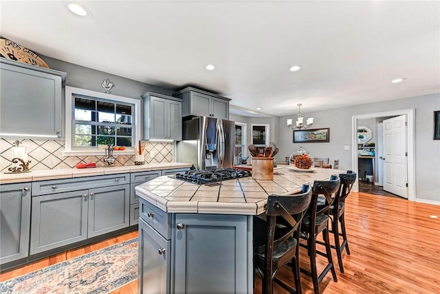 kitchen featuring tile countertops, black gas cooktop, gray cabinetry, a kitchen island, and stainless steel fridge with ice dispenser