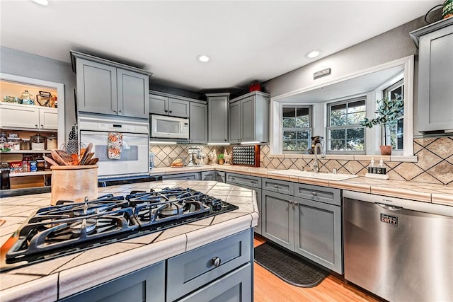 kitchen with tile countertops, light wood-style flooring, white appliances, a sink, and gray cabinets