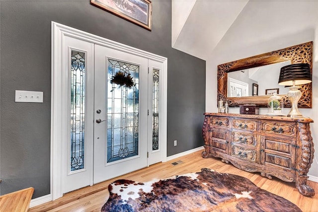 foyer entrance with visible vents, baseboards, vaulted ceiling, and wood finished floors