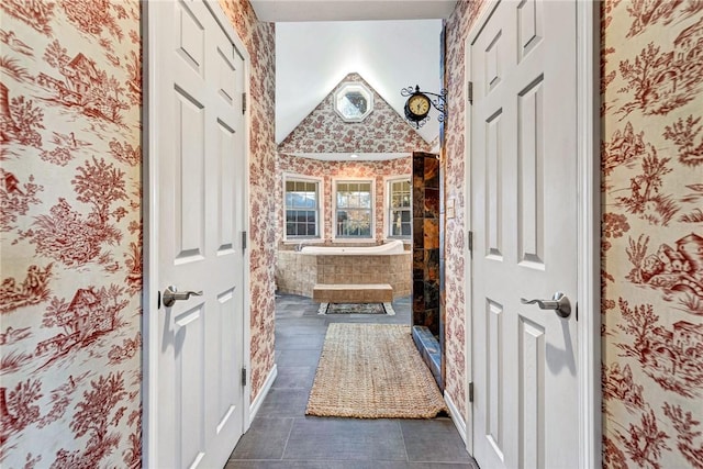 full bath featuring tiled shower, vaulted ceiling, and wallpapered walls