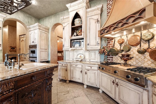 2 S Samoset Ct, Rogers, AR 72758 - kitchen featuring arched walkways, stainless steel appliances, backsplash, custom exhaust hood, and cream cabinets