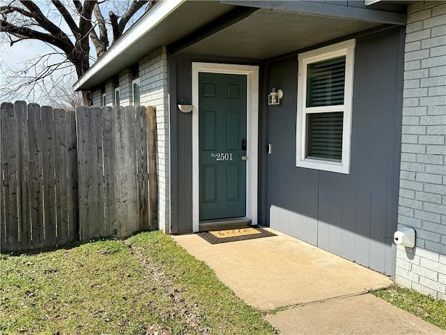 view of exterior entry with brick siding and fence