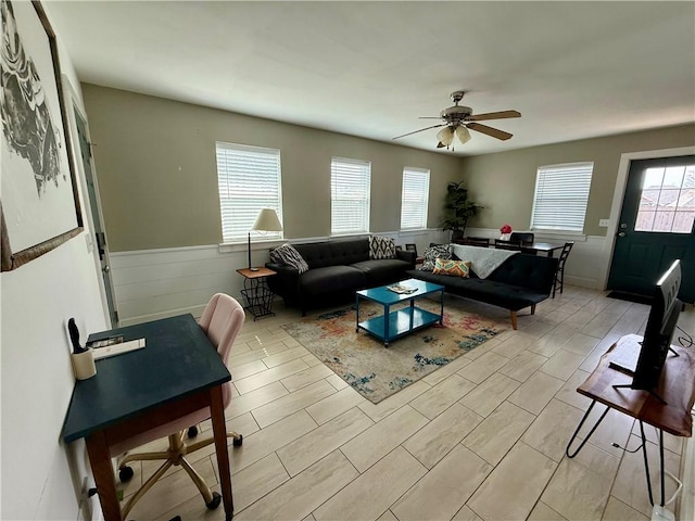 living room with a ceiling fan and a wainscoted wall