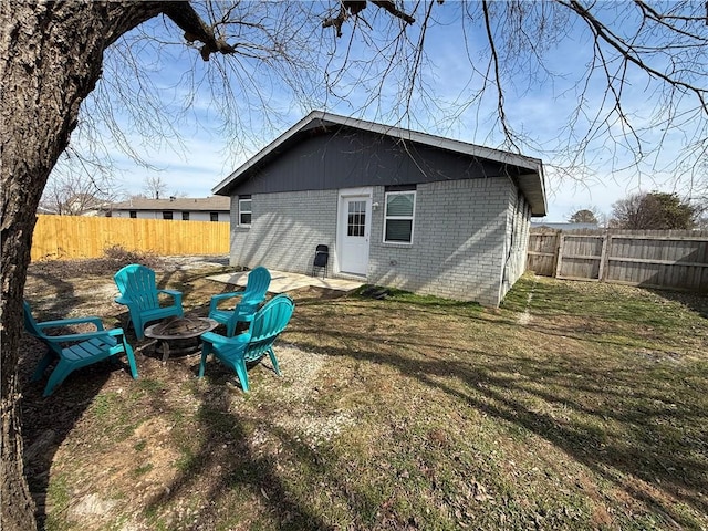 back of house with brick siding, a lawn, a fire pit, and a fenced backyard