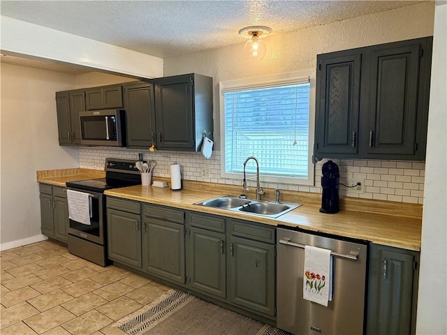 kitchen with light countertops, backsplash, appliances with stainless steel finishes, a sink, and a textured ceiling