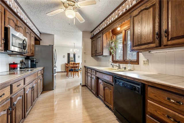 kitchen featuring a textured ceiling, a sink, appliances with stainless steel finishes, light wood-type flooring, and tile counters