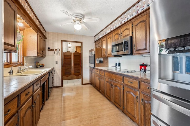 kitchen featuring light wood finished floors, tile countertops, a textured ceiling, black appliances, and a sink