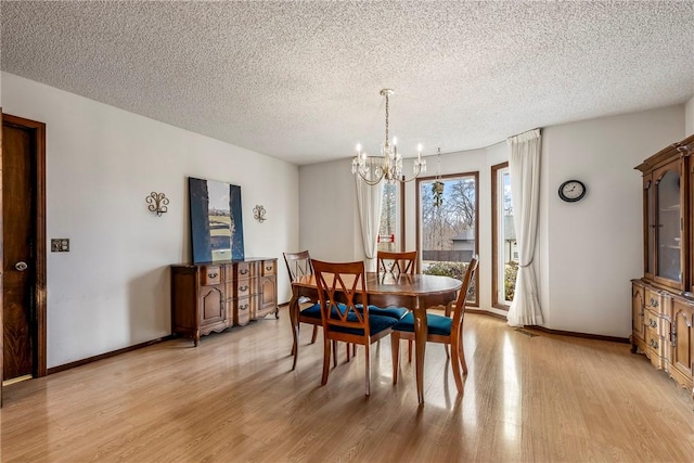 dining space featuring light wood-style floors, a notable chandelier, a textured ceiling, and baseboards