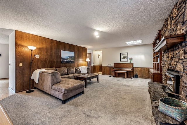 living room with a textured ceiling, a stone fireplace, wooden walls, a wainscoted wall, and light carpet