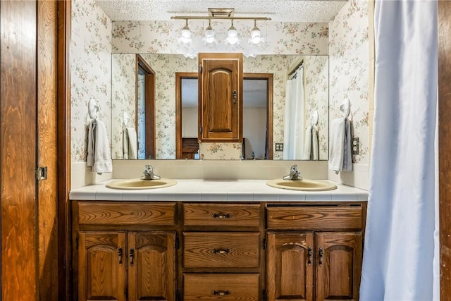 bathroom with a textured ceiling, a sink, and wallpapered walls