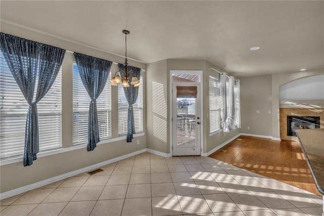 unfurnished dining area with visible vents, baseboards, a tile fireplace, an inviting chandelier, and tile patterned flooring