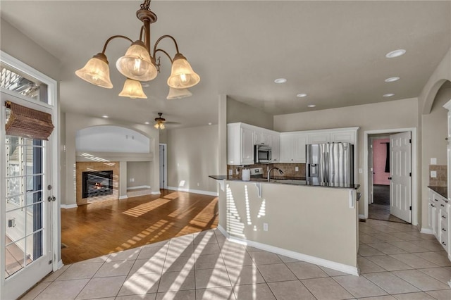 kitchen with light tile patterned floors, a tile fireplace, appliances with stainless steel finishes, decorative backsplash, and dark countertops