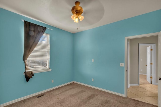 carpeted empty room featuring baseboards, visible vents, a ceiling fan, and tile patterned floors