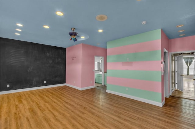 empty room featuring an accent wall, recessed lighting, baseboards, and wood finished floors