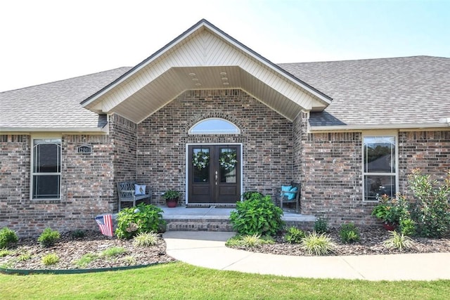 property entrance featuring a shingled roof, french doors, and brick siding