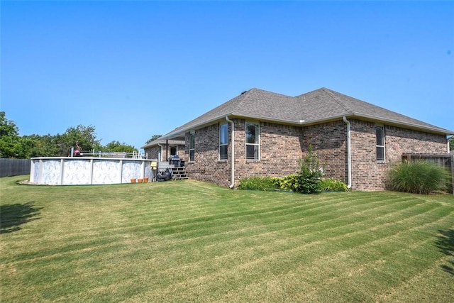 view of home's exterior featuring an outdoor pool, a lawn, roof with shingles, fence, and brick siding