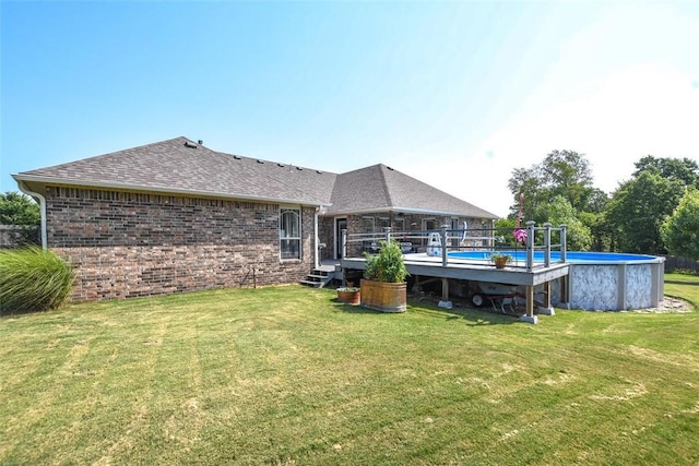 rear view of house with brick siding, a shingled roof, a lawn, an outdoor pool, and a wooden deck