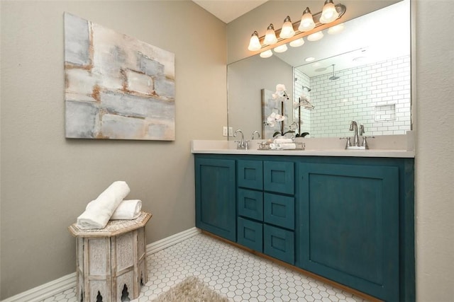 bathroom featuring a sink, double vanity, a tile shower, and baseboards