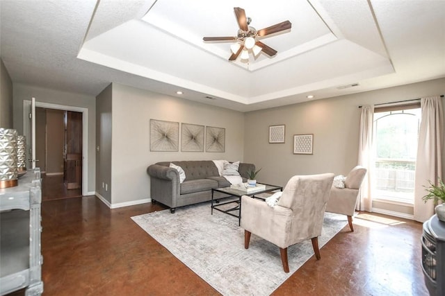 living room with a raised ceiling, visible vents, finished concrete floors, ceiling fan, and baseboards