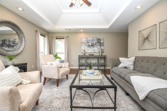 living room with recessed lighting, a tray ceiling, baseboards, and wood finished floors