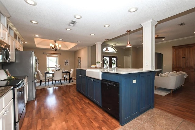 kitchen featuring blue cabinetry, a raised ceiling, appliances with stainless steel finishes, open floor plan, and ornate columns