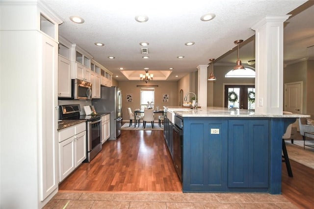 kitchen featuring appliances with stainless steel finishes, a tray ceiling, a kitchen bar, glass insert cabinets, and ornate columns