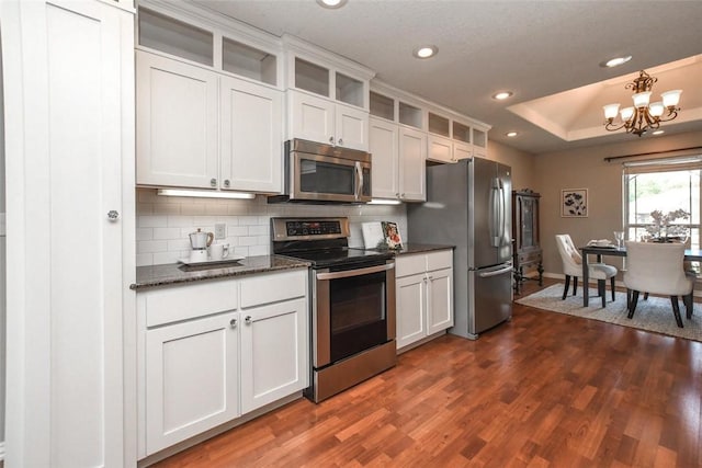 kitchen featuring dark wood-style floors, glass insert cabinets, appliances with stainless steel finishes, a tray ceiling, and backsplash