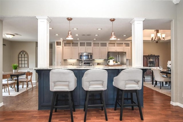 kitchen featuring appliances with stainless steel finishes, dark wood-style flooring, decorative light fixtures, and ornate columns