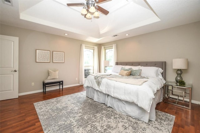 bedroom featuring baseboards, visible vents, a tray ceiling, and wood finished floors