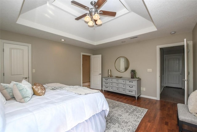 bedroom featuring dark wood-type flooring, a ceiling fan, visible vents, baseboards, and a tray ceiling