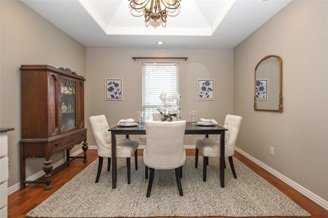 dining space featuring dark wood-style floors, a tray ceiling, baseboards, and a notable chandelier