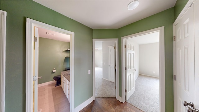 corridor with baseboards, visible vents, and wood finished floors