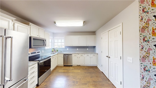 kitchen with appliances with stainless steel finishes, wood finished floors, white cabinetry, and decorative backsplash