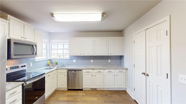 kitchen with light wood-type flooring, appliances with stainless steel finishes, decorative backsplash, and a sink