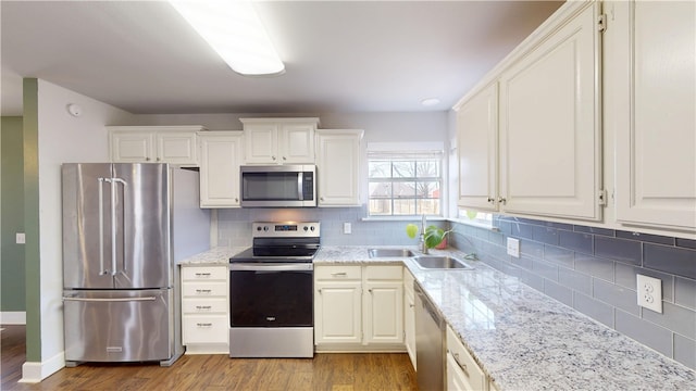 kitchen with tasteful backsplash, appliances with stainless steel finishes, wood finished floors, light stone countertops, and a sink