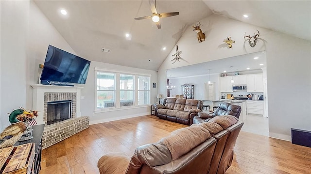 living room with light wood-type flooring, a fireplace, high vaulted ceiling, and a ceiling fan