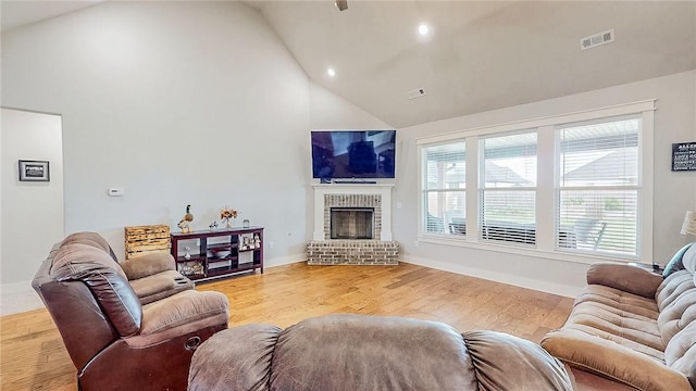 living area featuring high vaulted ceiling, a brick fireplace, visible vents, and wood finished floors