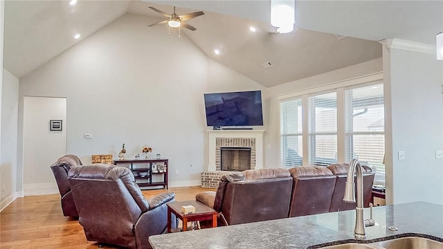 living room featuring light wood finished floors, a fireplace, high vaulted ceiling, and a ceiling fan