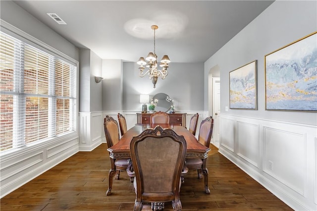 dining space featuring visible vents, dark wood-type flooring, a wainscoted wall, and a notable chandelier