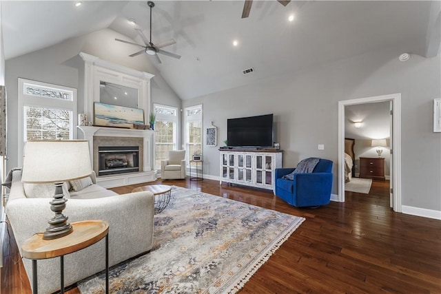 living room with hardwood / wood-style floors, visible vents, a fireplace with raised hearth, and ceiling fan