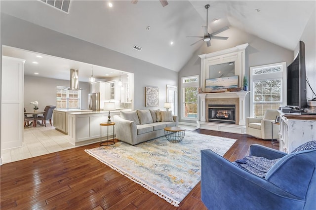 living room featuring visible vents, a lit fireplace, a healthy amount of sunlight, and light wood finished floors