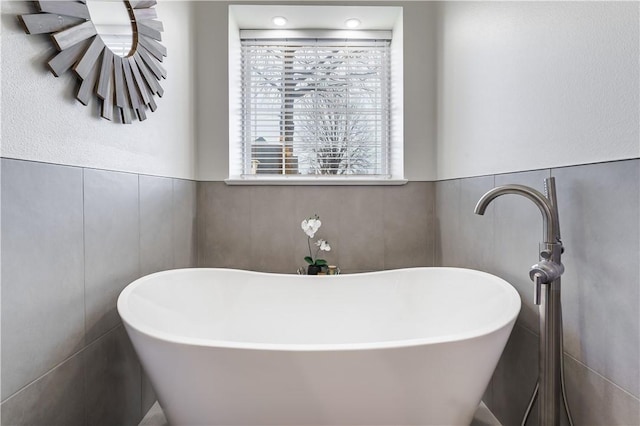 bathroom with a soaking tub, tile walls, and a wainscoted wall