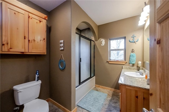 bathroom featuring toilet, shower / bath combination with glass door, baseboards, and vanity