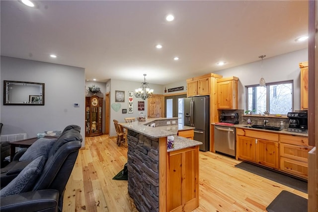 kitchen with light wood finished floors, appliances with stainless steel finishes, open floor plan, and a sink